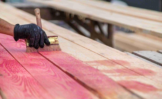 A professional painting red color staining on wood with black glove on him.