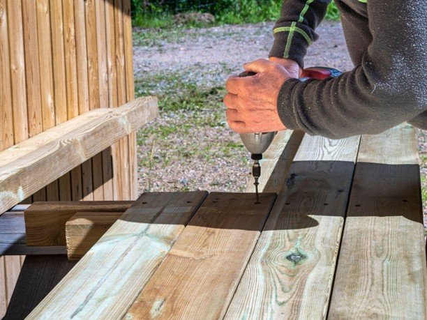 Contractor installing wooden deck boards with a power drill during a deck remodeling project.