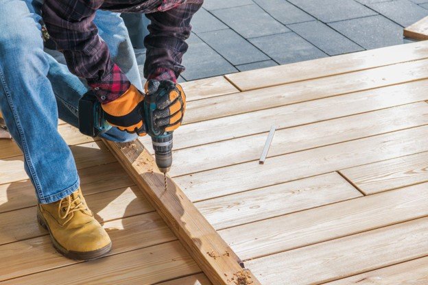Professional installing and securing new deck boards with a power drill.
