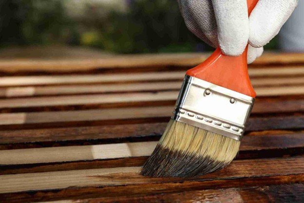Contractor applying fresh wood stain with a brush during a residential deck replacement project.
