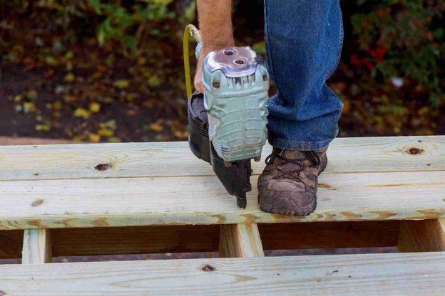 Professional deck builder fastening wood boards to the deck frame with a nail gun