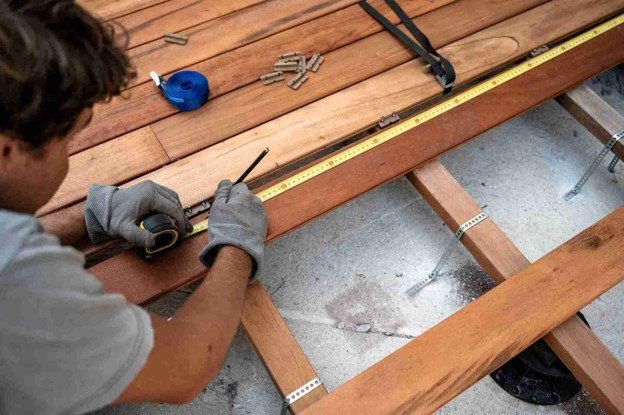 Deck contractor measuring wood boards during a residential deck repair and restoration project