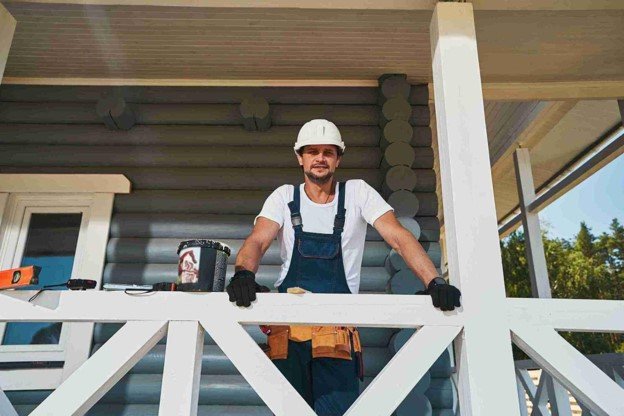 Professional deck contractor inspecting a repaired white wooden porch railing