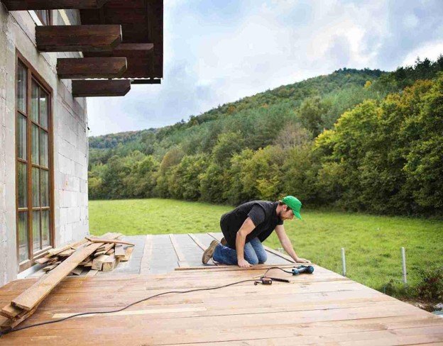 Contractor replacing old deck boards with new wood decking at a residential property