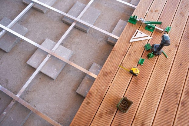 Custom deck under construction with metal framing, wood decking, and professional installation tools.