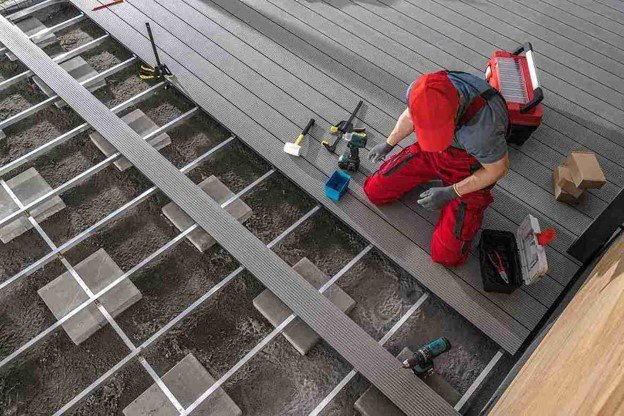 Professional deck installer working on a residential rooftop deck with construction tools and materials.
