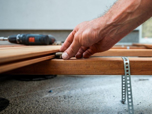 Close-up of a deck installer securing wood decking boards to the frame with hidden fasteners